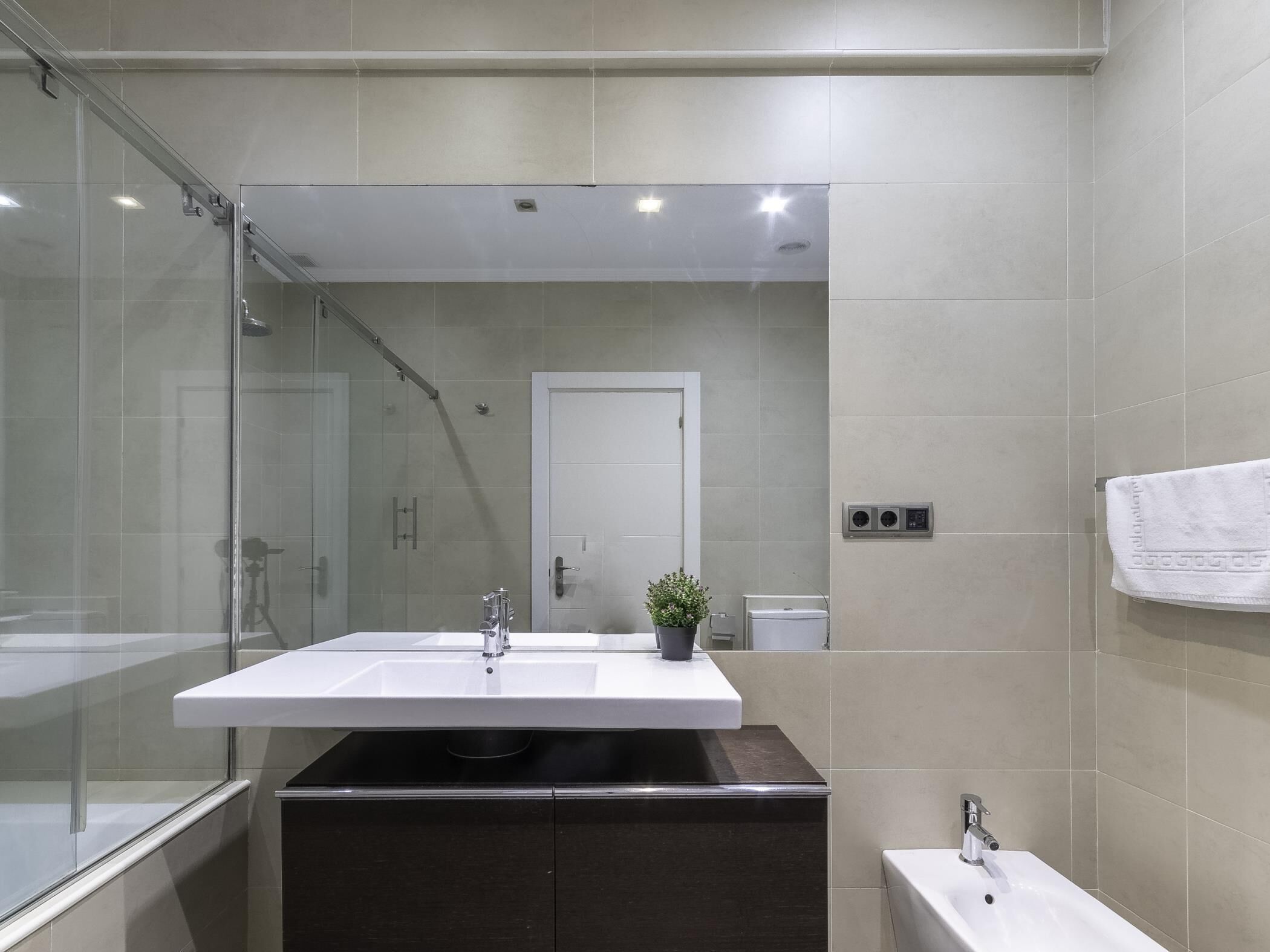 Un baño moderno con cabina de ducha de vidrio, tocador doble y una toalla blanca colgada en la pared.