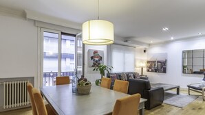 A modern living room with a dining area, featuring a large table, comfortable seating, and a cityscape painting. - Spacious and cosy in a central neighbourhood, Indautxu. (Bilbao)