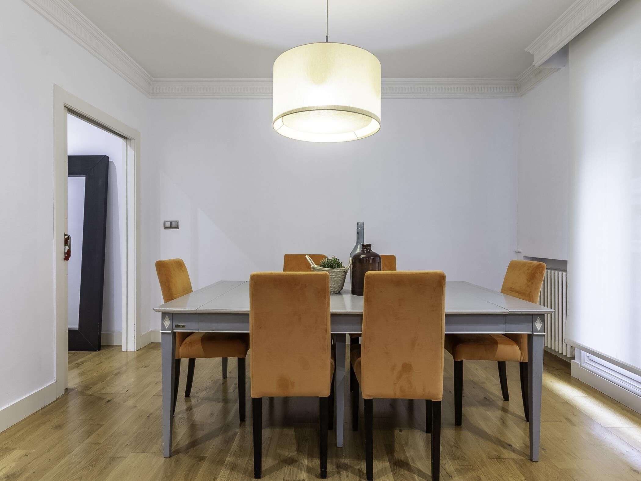 Un comedor con una mesa rectangular, seis sillas, una lámpara colgante y una planta en maceta.