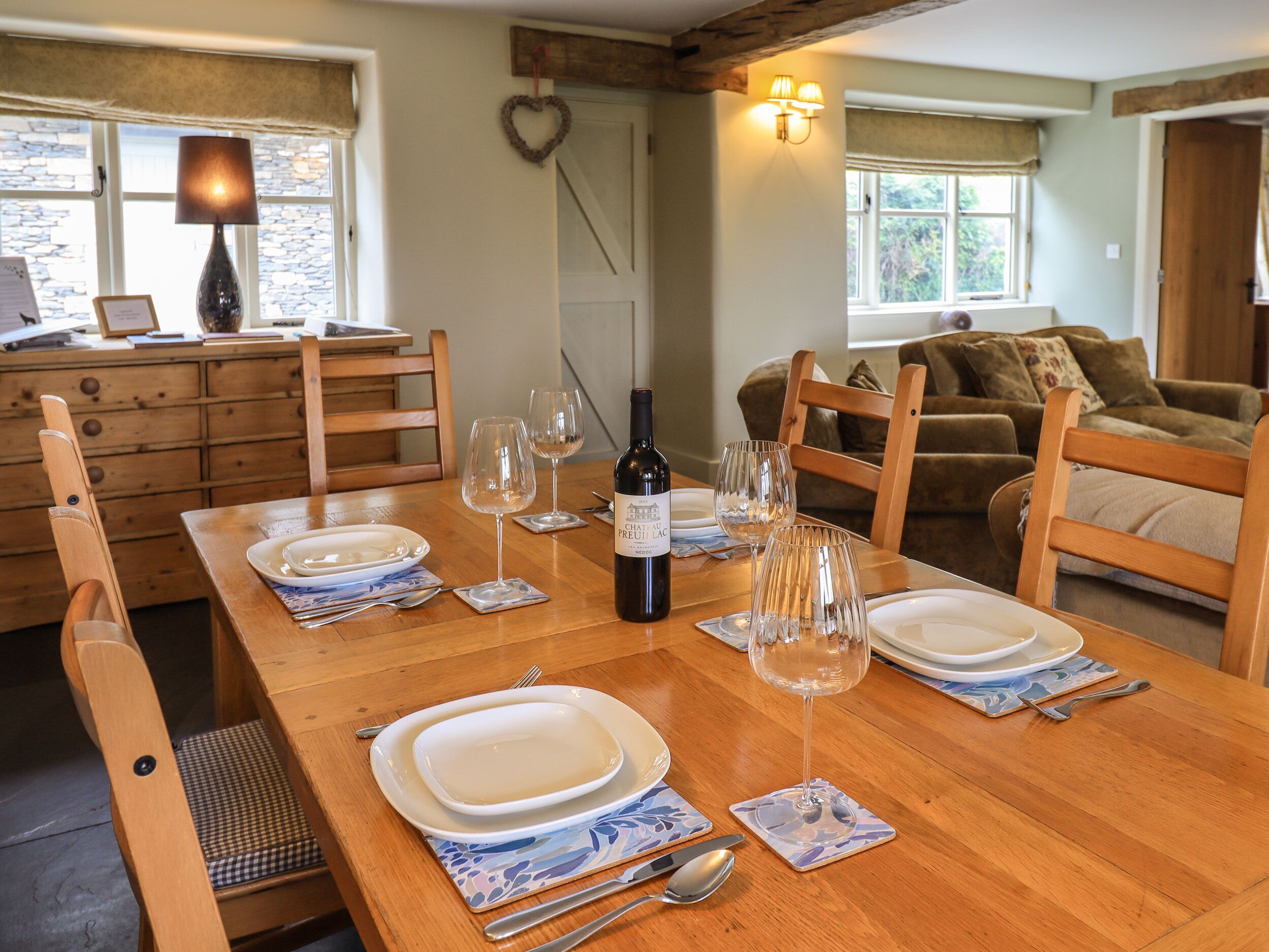 A dining table set with plates, wine glasses, and cutlery, with a bottle of wine in the center.