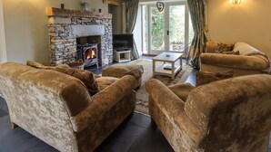 Una sala de estar acogedora con chimenea de piedra, sofás cómodos, un televisor de pantalla plana y vistas al verdor a través de amplios ventanales.
