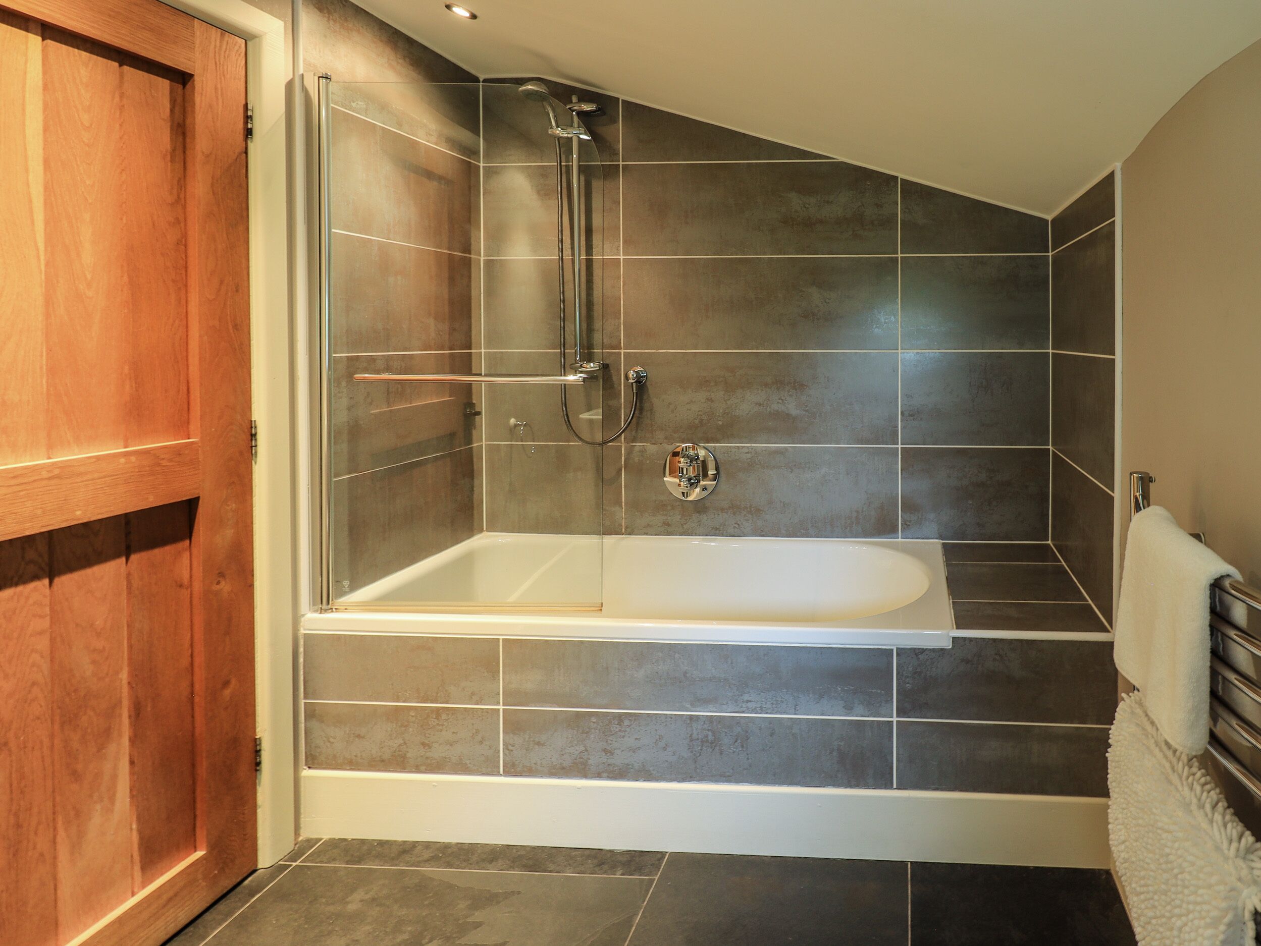 A modern bathroom with a glass-enclosed shower, a freestanding bathtub, and dark tiled walls.