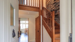 Un pasillo con escalera de madera, pared de piedra y un área de comedor al fondo.