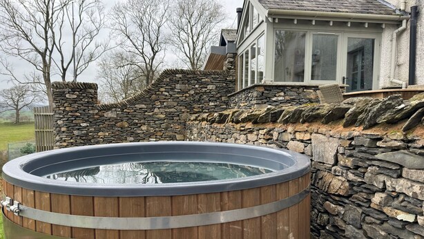 Un muro de piedra con un jacuzzi de madera al frente.