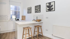 A modern kitchen with white cabinetry, a central island with stools, and abstract wall art.