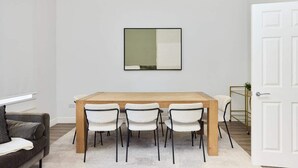 A dining area with a wooden table and four chairs, a white wall with a framed artwork, and a white door.