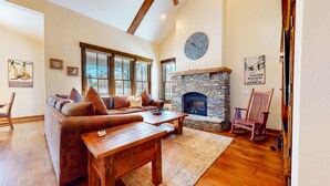 A cozy living room with a stone fireplace, wooden furniture, and large windows. - Snowcreek Vi The Lodges #1167 4 Bedroom Condo by RedAwning (Mammoth Lakes)