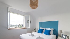 A bedroom with a large bed, a window with a view, and a blue accent wall.