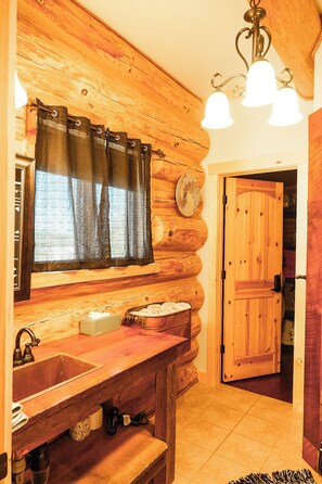 A log cabin interior with a wooden sink, a window with curtains, a door, and a chandelier. - Handcrafted Log Cabin | Hot Tub | Sauna | GameRoom (Ironwood Township)