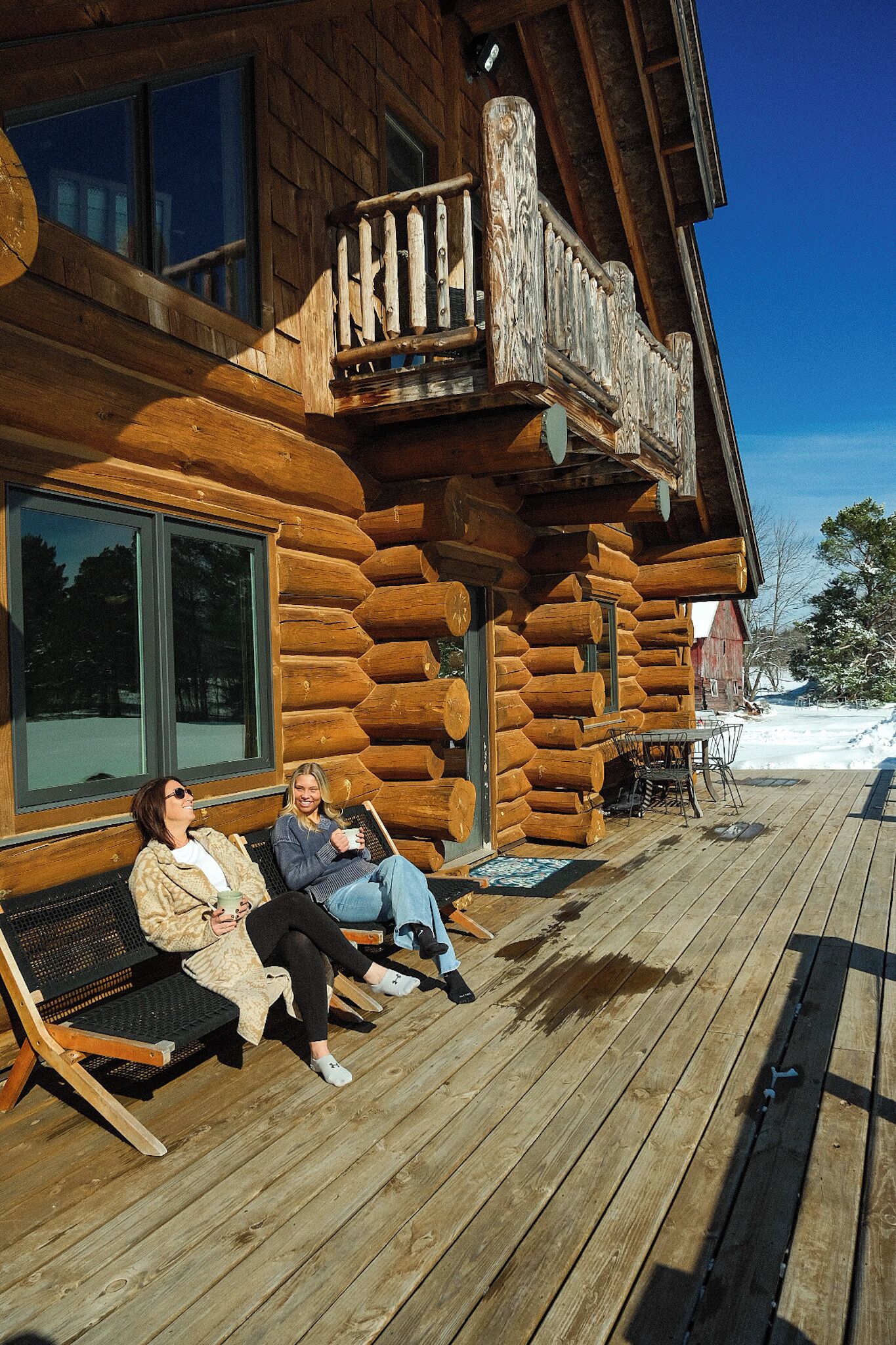 A log cabin with a wooden deck, large windows, and a visible outdoor seating area.