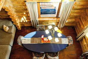 A wooden cabin interior with a round table, patterned chairs, a sofa, and a window with curtains. - Handcrafted Log Cabin | Hot Tub | Sauna | GameRoom (Ironwood Township)