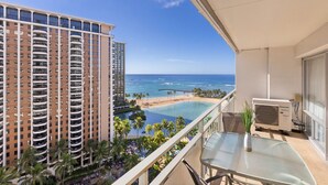 Un balcón con vista a una playa y al océano, una piscina y un edificio alto al fondo.