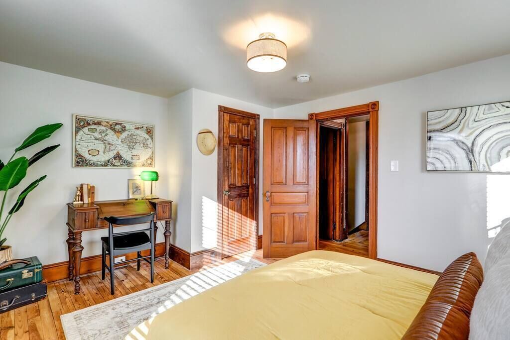 A bedroom with a bed, wooden desk, chair, and a large plant.