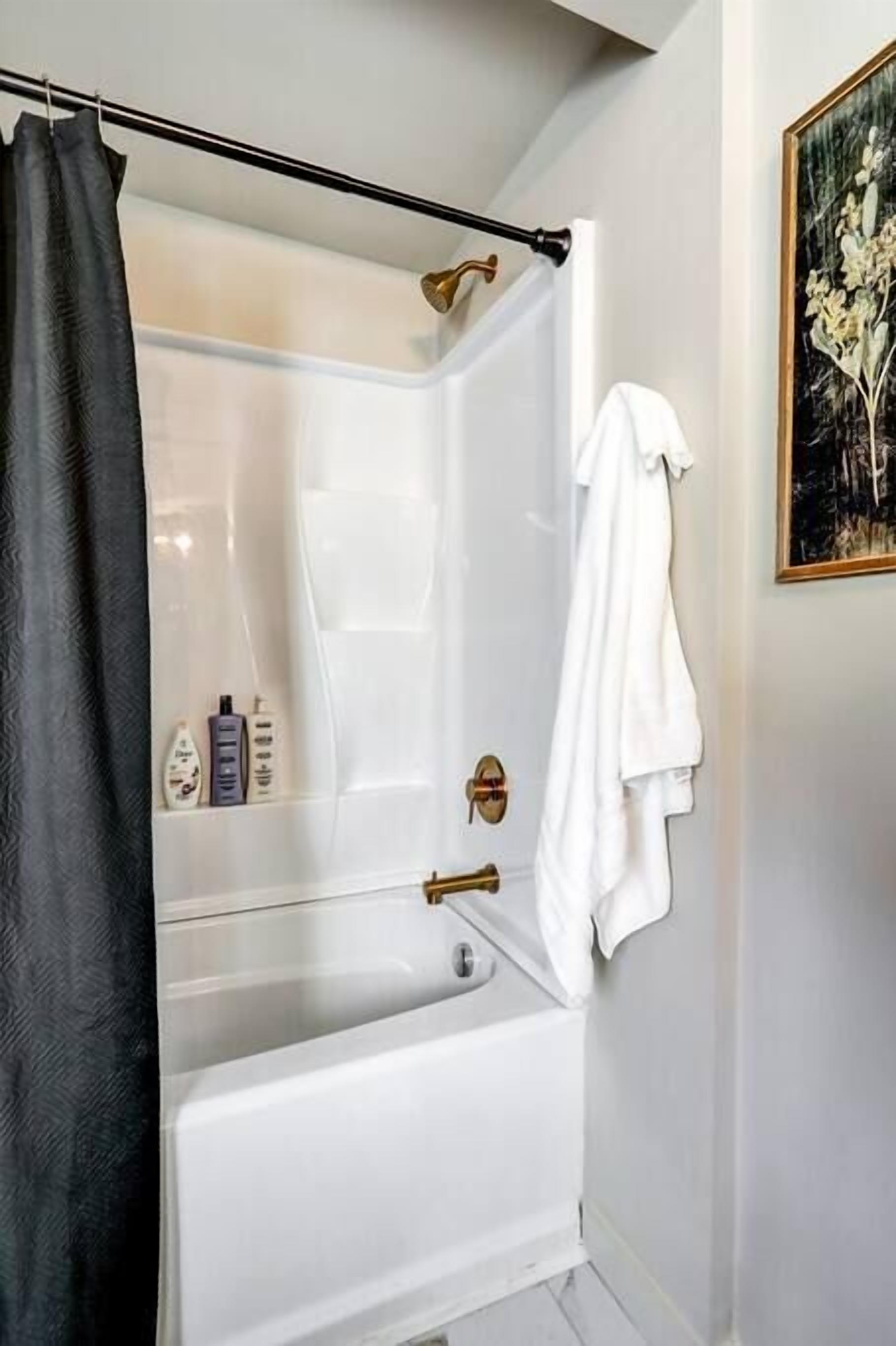 A bathroom with a bathtub, a shower curtain, a towel rack, and a framed picture on the wall.