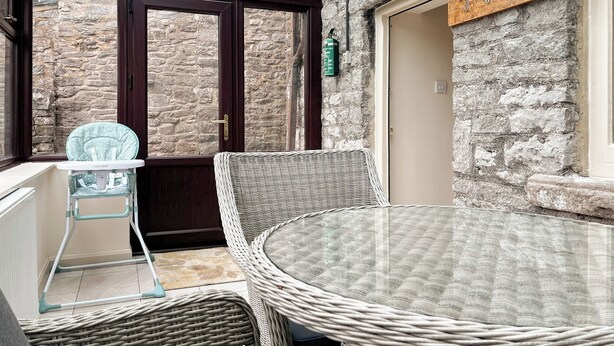 A cozy patio area with wicker furniture, a baby high chair, and a stone wall. - 2 bedroom accommodation in Monyash (Monyash)