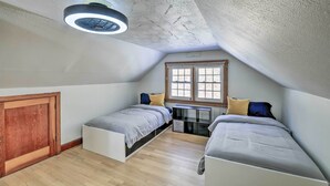 Ein kleines, modernes Schlafzimmer im Dachgeschoss mit zwei Betten, einer Holztür, einem Fenster und einem Deckenventilator.