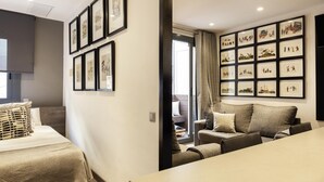 A modern hotel room with a bed, a sofa, and a dining table. There are framed pictures on the walls and a window with curtains. - Sophisticated Flat in Trendy Poble Sec (Barcelona)