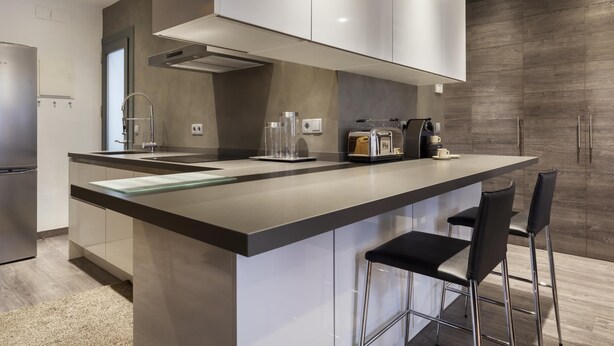 A modern kitchen with a central island, stainless steel appliances, and bar stools. - Sophisticated Flat in Trendy Poble Sec (Barcelona)