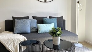 Un salon moderne avec un canapé gris, des coussins à motifs, une table basse ronde sur laquelle est posée une plante en pot et un lampadaire.