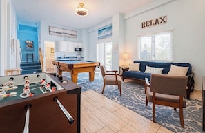 Un salon avec un baby-foot, un canapé et un panneau indiquant « RELAX » au mur.