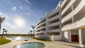 Een modern hotel met een zwembad, meerdere balkons en een heldere lucht.
