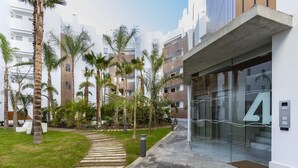 Een modern gebouw met glazen ingang, palmbomen en een verhard pad.