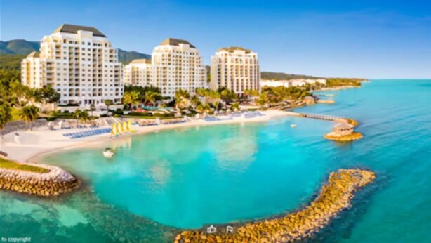 Ein Küstenhotel mit mehreren Hochhäusern, einem Strand und klarem, türkisblauem Wasser.