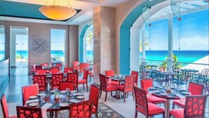 Ein Restaurant mit roten Stühlen und Tischen, großen Fenstern und Blick auf den Ozean.