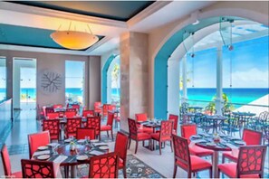 A restaurant with red chairs and tables, large windows, and a view of the ocean. - Spectacular 3BR 3.5BA -optional all-inclusive resort high floor beachfront tower (Montego Bay)