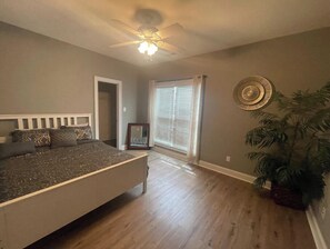 A bedroom with a bed, a ceiling fan, a window with blinds, and a plant.