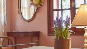 A room with a bed, a wooden nightstand with a potted plant, a mirror, a window with curtains, and a lamp. - Kalivia House - Entire Home (Skoutari)