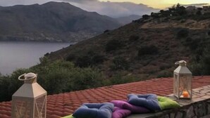 A stone wall with colorful cushions and two lit lanterns overlooking a mountainous landscape and a body of water. - Kalivia House - Entire Home (Skoutari)