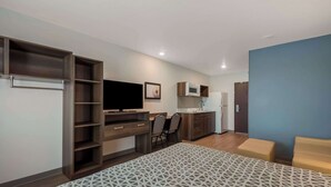 A compact room with a bed, a TV, a desk, and a kitchenette.