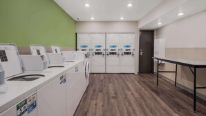 A laundry facility with multiple washing machines and dryers, a table, and a green wall.