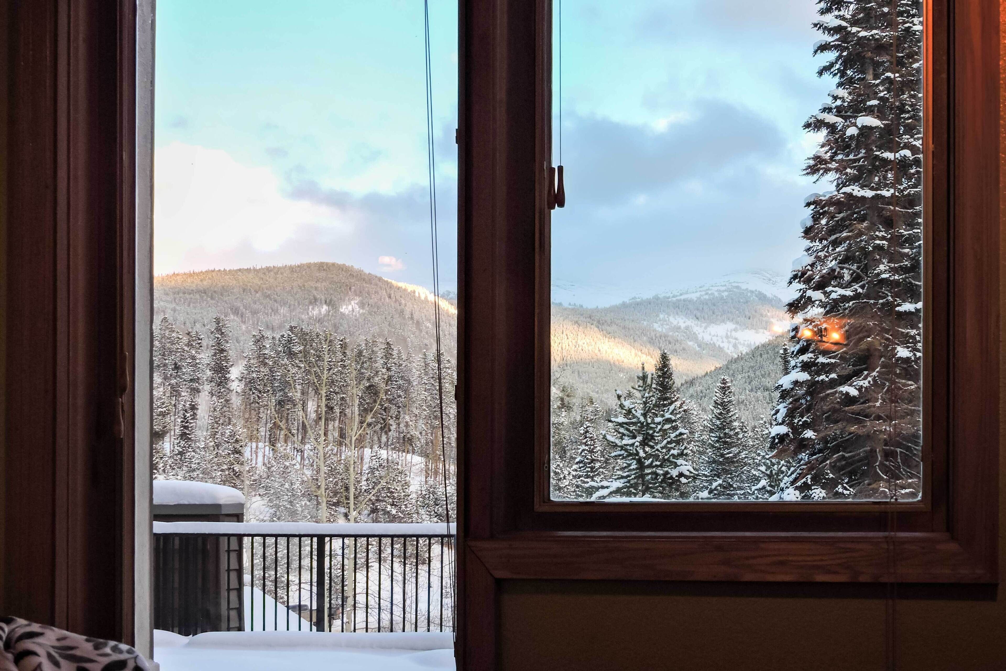 A room with a large window offering a view of a snowy mountain landscape.