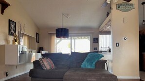 A living room with a gray sofa, a teal throw pillow, and a wooden floor. - Spacious home with Tranquil backyard (Aurora)