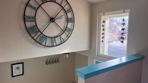 A room with a large wall clock, a framed picture, and a window with hanging decorations. - Spacious home with Tranquil backyard (Aurora)
