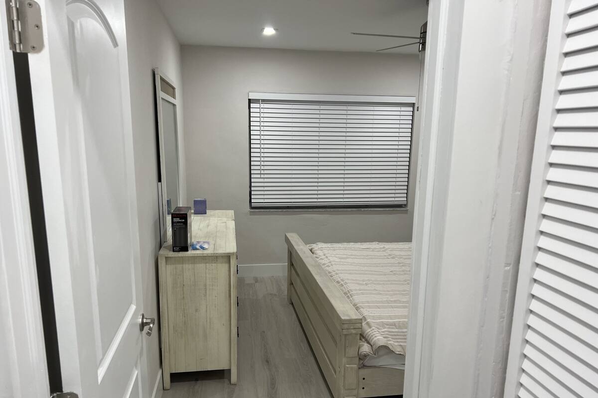 Une petite chambre à coucher avec un lit, un bureau et une fenêtre équipée de stores.