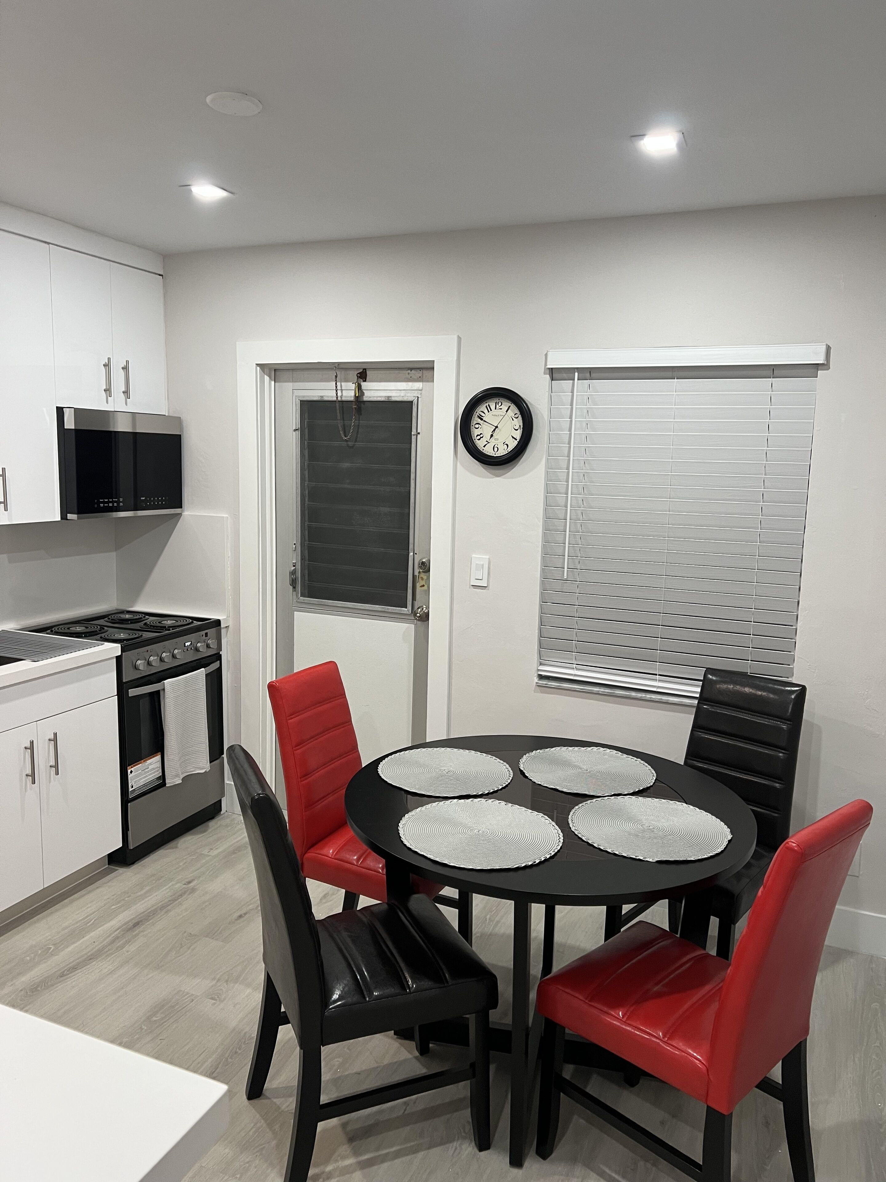 A modern kitchen with white cabinets, a black stove, and a dining area with a round table and red chairs.