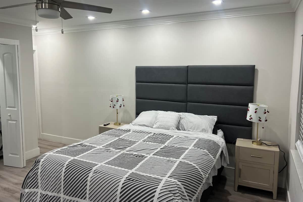 Une chambre à coucher moderne, comprenant un lit, deux tables de chevet, un ventilateur de plafond et une petite table de nuit avec une lampe.