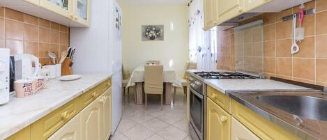 A kitchen with yellow cabinets, a white refrigerator, a dining table with chairs, and a stove.