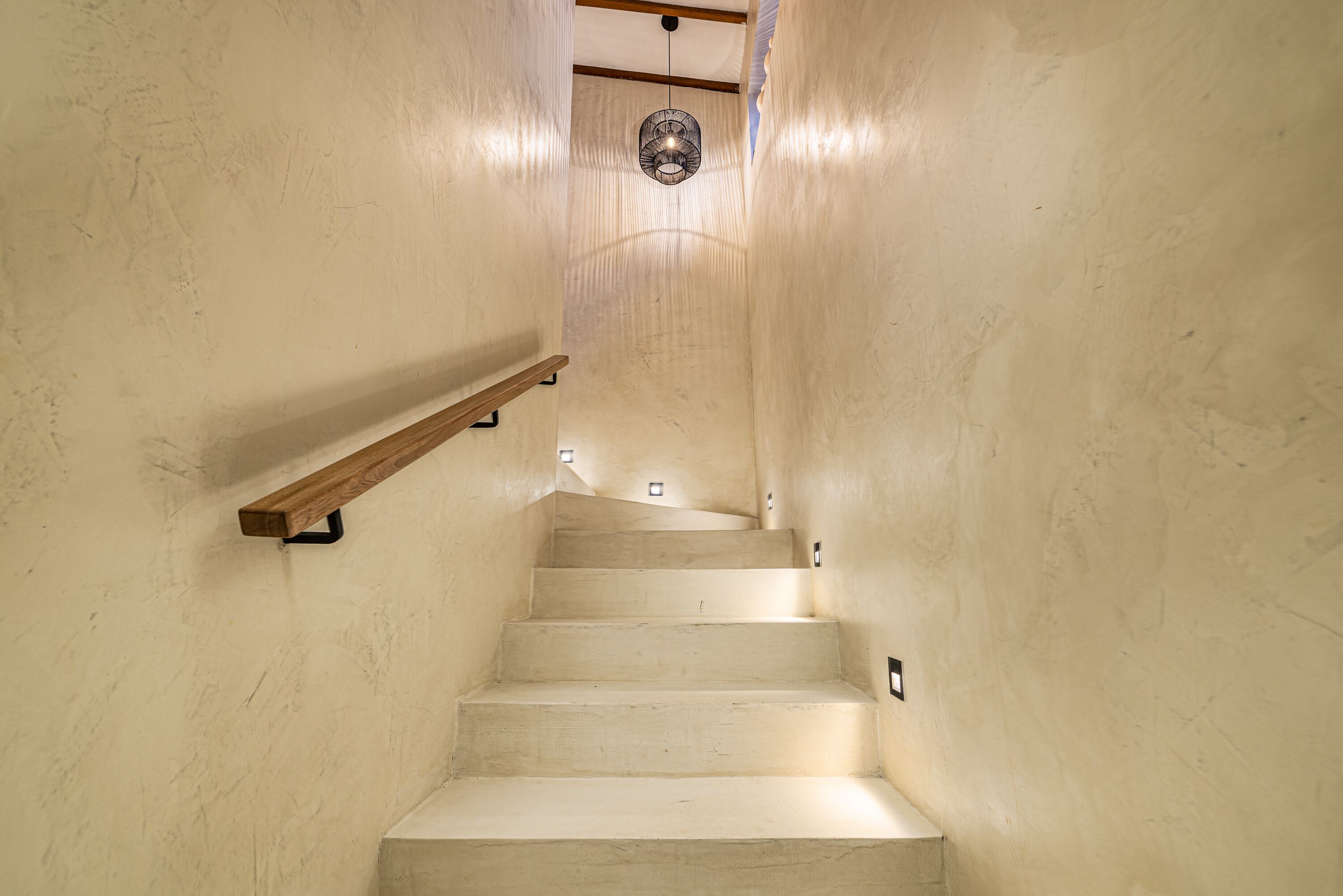 Un escalier étroit avec une rampe en bois et un luminaire suspendu en haut.