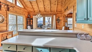 L’intérieur d’un chalet en bois comprend un coin cuisine, de grandes fenêtres et un lustre.