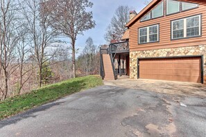 Une cabane en rondins à deux étages, dotée d’une façade en pierre, d’une terrasse en bois et d’un garage.