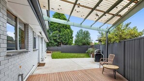 Une terrasse couverte avec une plateforme en bois, un barbecue et un coin salon comprenant deux chaises.