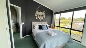 Une chambre avec un grand lit, une vue sur l’extérieur et une porte donnant sur une autre pièce.