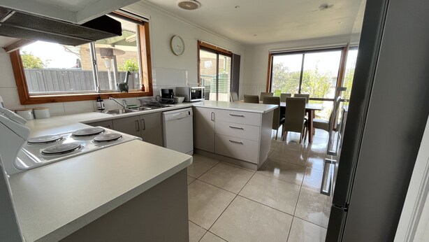 Une cuisine moderne avec des meubles blancs, une cuisinière encastrée et un coin repas comprenant une table et des chaises.