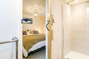 A room with a bed, a shower, and a wall with a brick pattern. - The Old Bakehouse - Within the Helland Barton Farm Collection (Delabole)