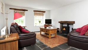 A cozy living room with leather sofas, a wooden coffee table, a red lamp, a television, and a stone fireplace.