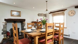 A dining area with a stone fireplace, wooden chairs, a wooden table set for four, and a clock on the wall.